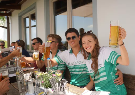 Man and women wearing a bicycle jersey, holding up glasses full of beer