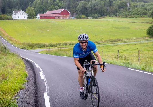 Man riding bike on asphalt road through a grassy field