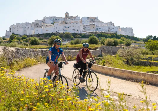 Two women riding bikes with an ancient building in the background