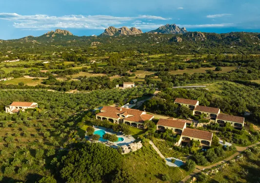 Sky view of brown and yellow building in the middle of a valley of trees