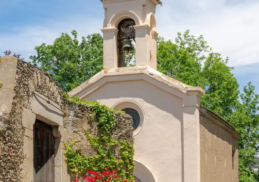 Woman in green jacket riding a bike in front of a church with a small bell tower