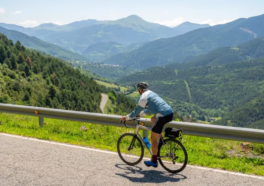Man riding a bike on a road, with large valleys of trees in the distance with large hills