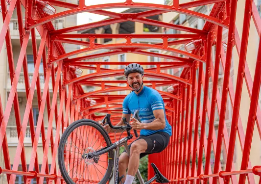 Man balancing on one wheel on a bike, in the middle of a red bridge