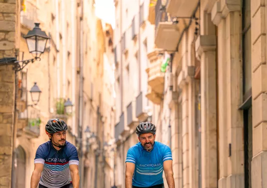 Two men biking through a rustic town on a stone pathway