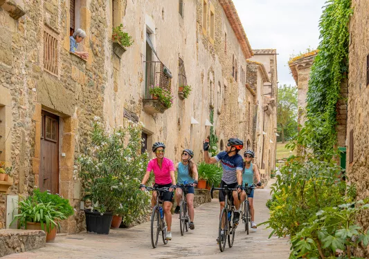 Group of 4 people riding their bikes in an alleyway of a rustic town, surrounded by stone buildings