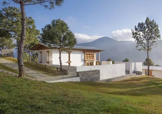 White building on a hill surrounded by trees with mountains in the distance