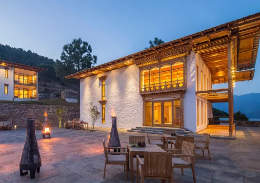 White building with a wooden balcony and outdoor patio area with tables and chairs