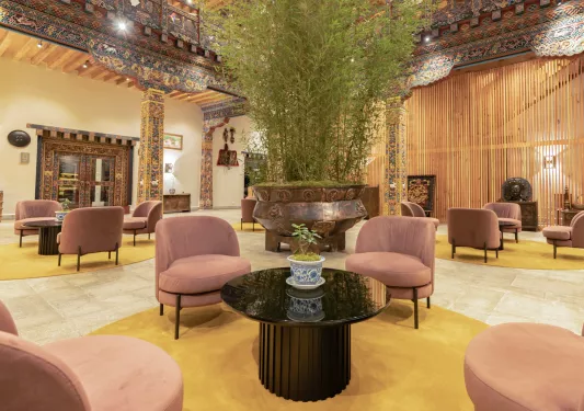 Indoor hotel lobby with pink, cushioned chairs and a large plant in he center