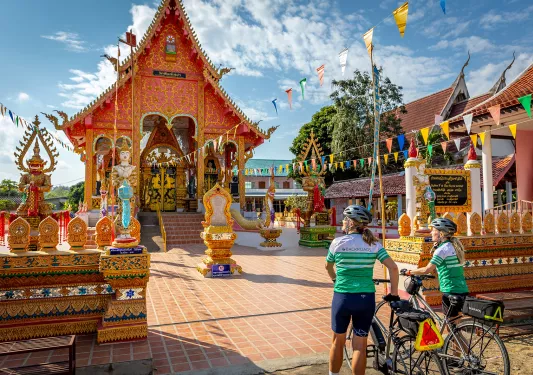 Two women walking their bikes as they approach a shrine
