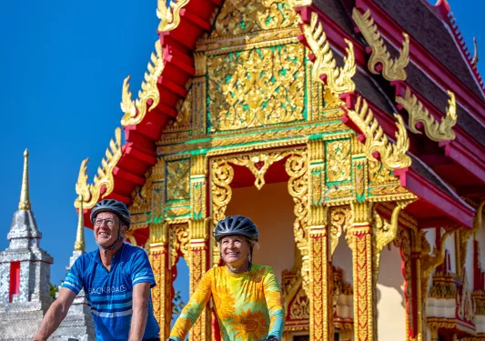 Two people biking in front of a colorful temple