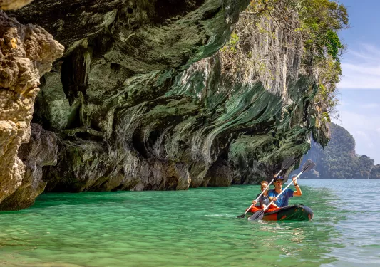 Man and woman paddling in a red kayak in the ocean, under a cliff