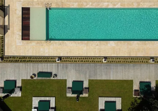 Sky view of an outdoor pool with green pool chairs and grass areas surrounding the pool