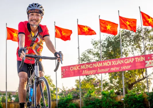 A man smiles while biking in front of a row of red flags