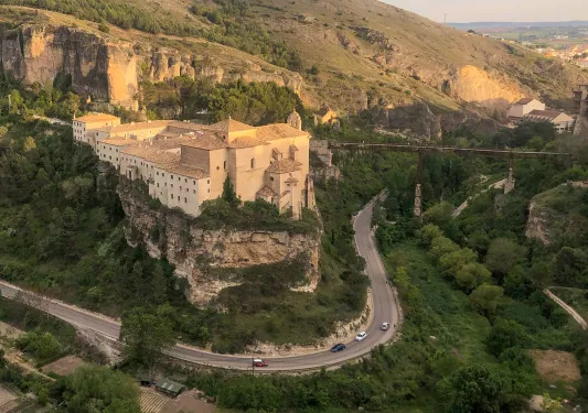 Stone, rustic building on a cliff, next to a road with a sharp curve
