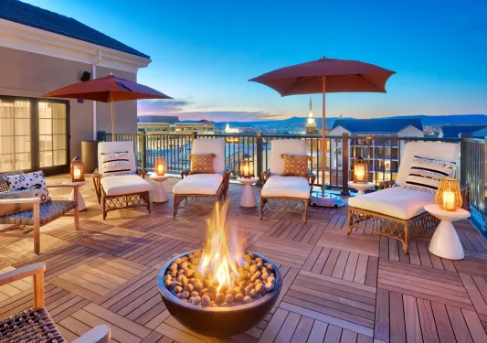 Wooden balcony with white chairs surrounding a stone firepit