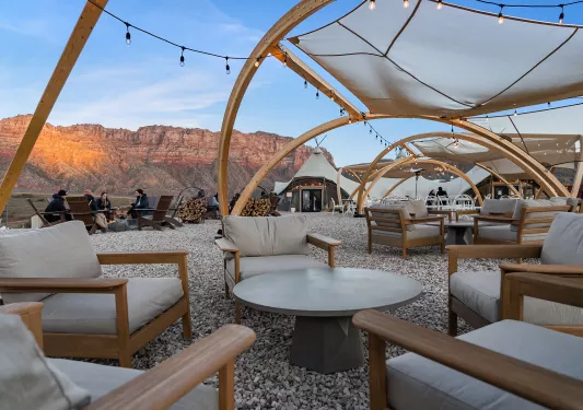Gray, cushioned seats around a circular table on gravel, with large canyons in the background