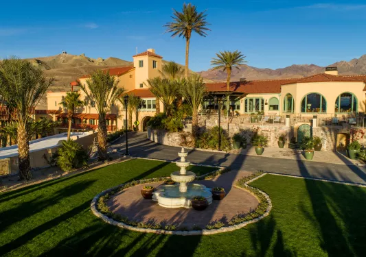 Exterior vide of tan and brown building, with a garden and circular fountain in front