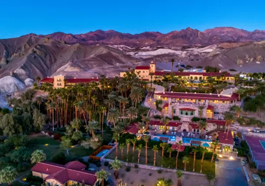Exterior, sky view of tan and red hotel buildings, with tall palm trees and outdoor pool