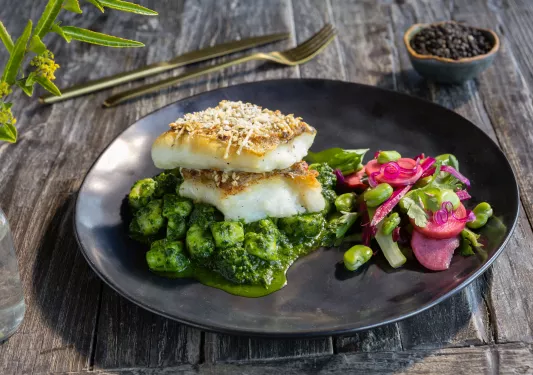 Black plate with grilled fish on top of a bed of green and pink vegetables