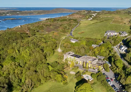 Sky view of large hotel building in the middle of a grass valley, surrounded by lush trees