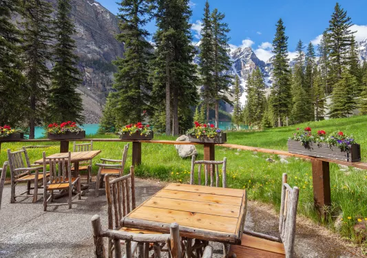 Outdoor patio with wooden chairs and tables, looking out to a lake surrounded by trees