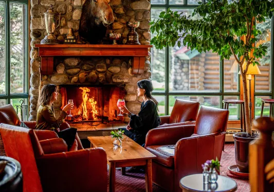 Two women holding wine glasses next to a stone fireplace
