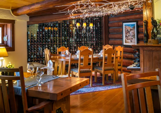 Dining room with wooden tables and chairs next to a large wine cellar