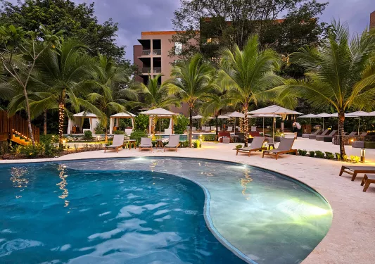 Outdoor pool with white chairs with a hotel in the background