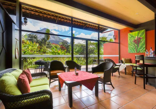 Bar and lounge with woven chairs and large glass walls and doors leading to a jungle