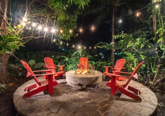 Red lawn chairs surrounding a stone fire pit outdoors on a circular rock slab