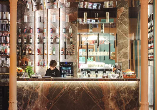 Liquor bar with stone countertops and brown pillars, with a bartender behind the counter