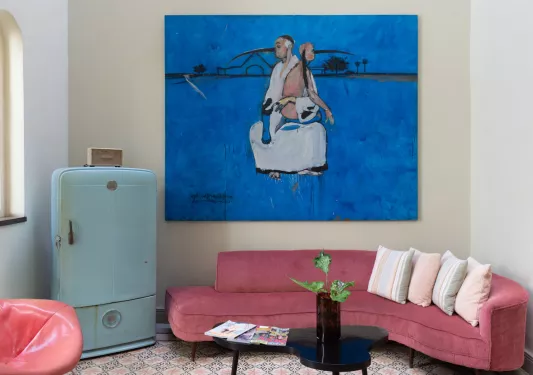 room with red couch, blue fridge, and large blue painting