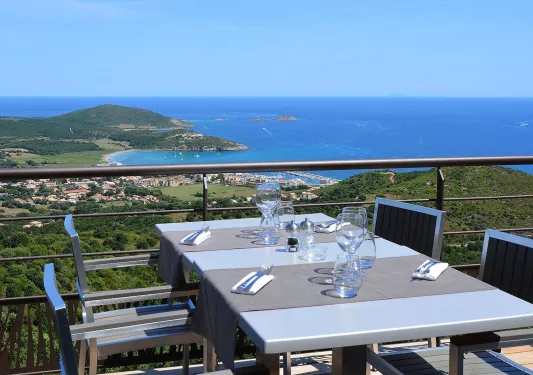 Dining table on a balcony, overlooking the ocean and a small town in the distance