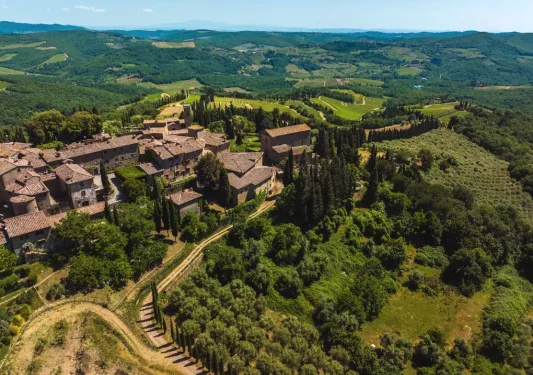 Sky view of brown brick buildings surrounded by a valley of trees and crops