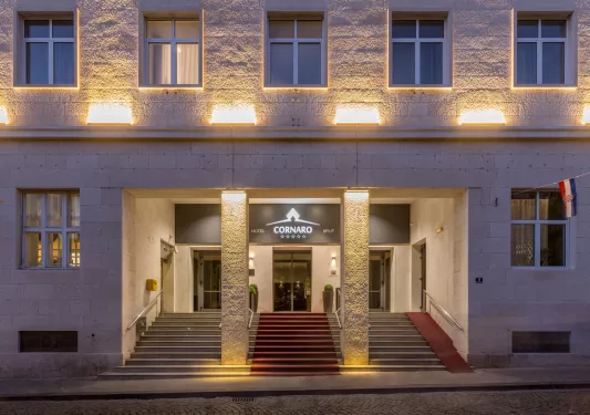 Hotel building entrance, with lights illuminating the stone wall and a red carpet on the stairs
