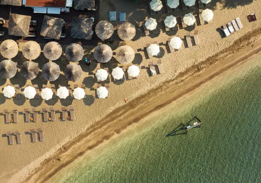 Sky view of beach with white and tan umbrellas on the sand