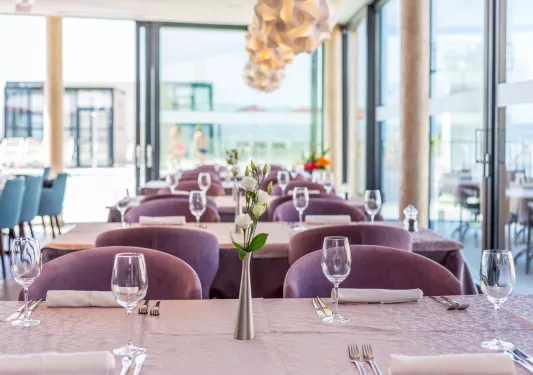Dining hall with pueple, cushioned chairs and a vase with flowers in the center of the table