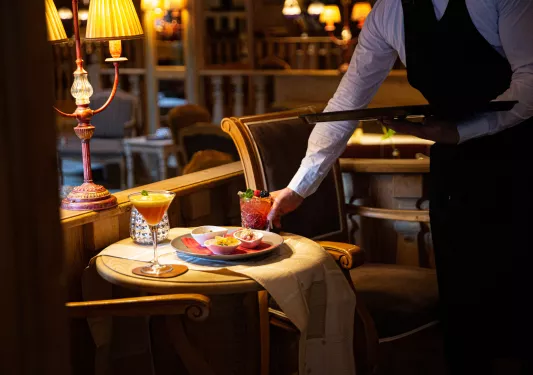 Waiter serving a red drink and a plate of food to an empty, circular table