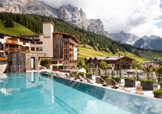 Outdoor infinity pool overlooking a hotel complex and tall, tree-covered hills