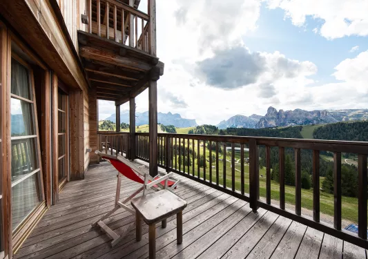 Wooden balcony with a red chair looking out towards cloud-covered mountains