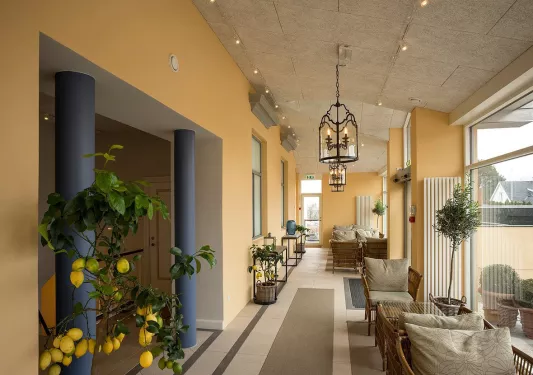 Hallway with tables and chairs and a lemon tree between two blue pillars