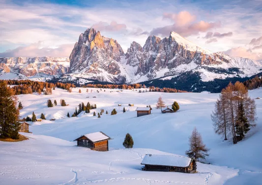 A snowed in plain with small houses and mountains in the background
