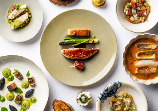 4 plates full of fancy arranges of seafood, soup, and small bites