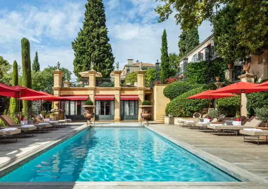 Outdoor pool with a yellow building in the background, with red umbrellas surrounding the pool