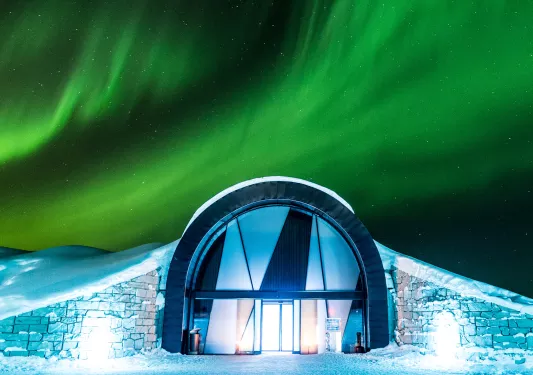 Entrance of building in the middle of a snow valley, with the Northern Lights in the sky