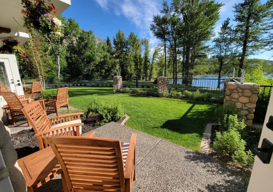 Wooden chairs in a stone patio, looking out to a grass field and a lake surrounded by trees