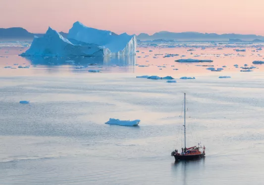 a ship floating on reflective water during a pink sunset