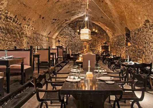Indoor dining area with large, stone walls and light fixtures hanging from the ceilings