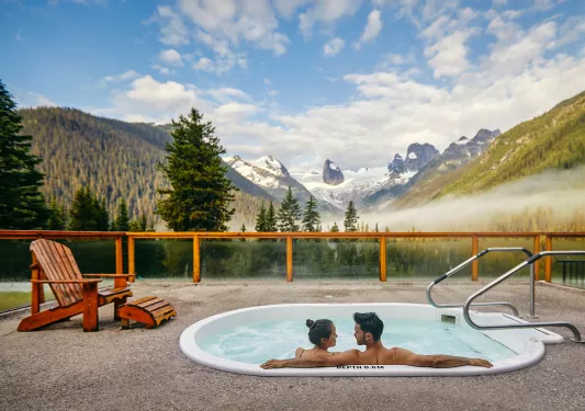 two people in a hot tub overlooking snow capped mountains