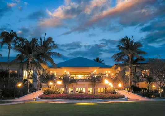 Hotel entrance with a large grass area, surrounded by flowers and palm trees
